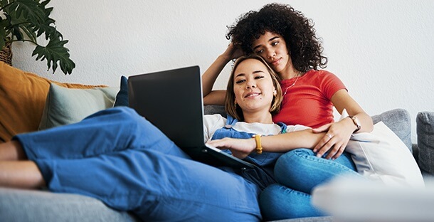 A couple cuddle on the couch, reviewing their finances on a laptop.