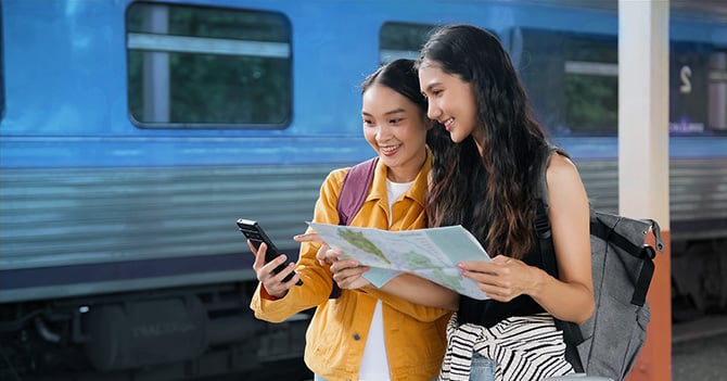 Two friends look at a map at a train station.