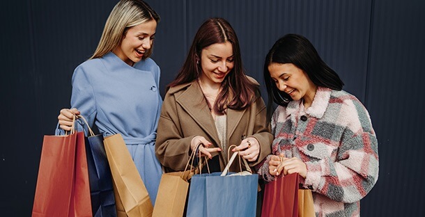A group of friends hold shopping bags and smile.