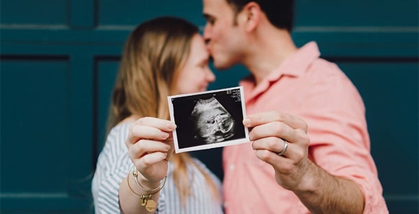 A couple embrace while holding their ultrasound picture.