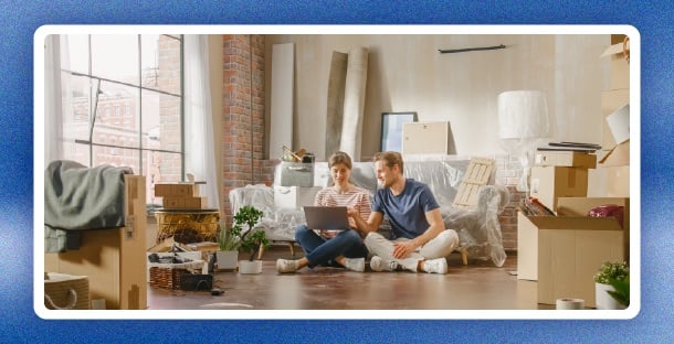 Two adults enjoying coffee together in their new home, surrounded by unpacked moving boxes.