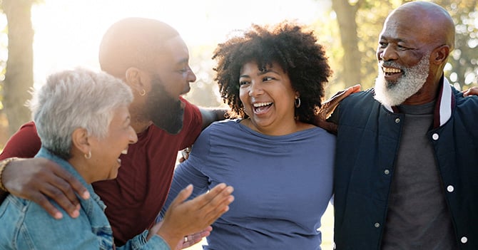 A diverse group of people chat and laugh while walking in the park.