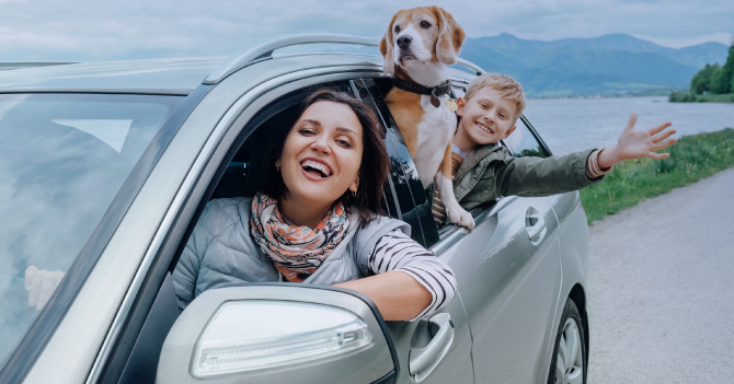 Woman and boy smiling from a car window with a dog.