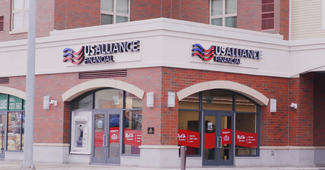USAlliance Financial branch with red brick exterior, arched windows, an ATM on the left, and red promotional banners.