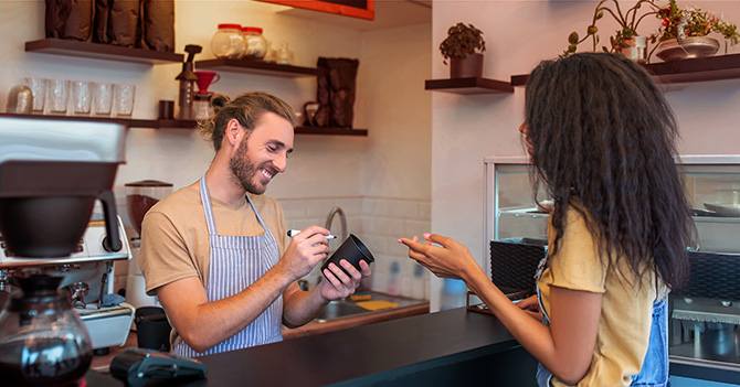 A woman gives her coffee order while a barista writes on a cup.