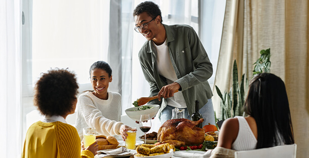 A man serves some Thanksgiving sidedish to his family sitting at the table.