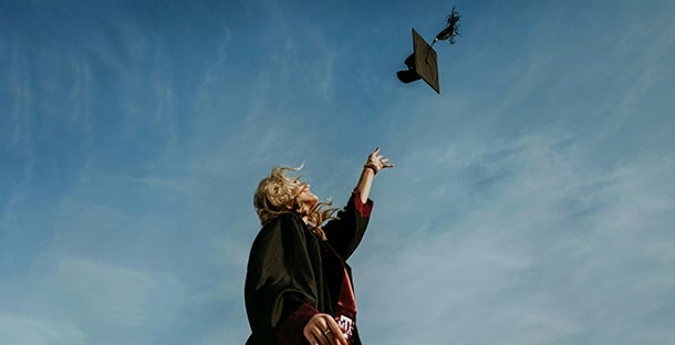 A student throws her graduation cap into the air.