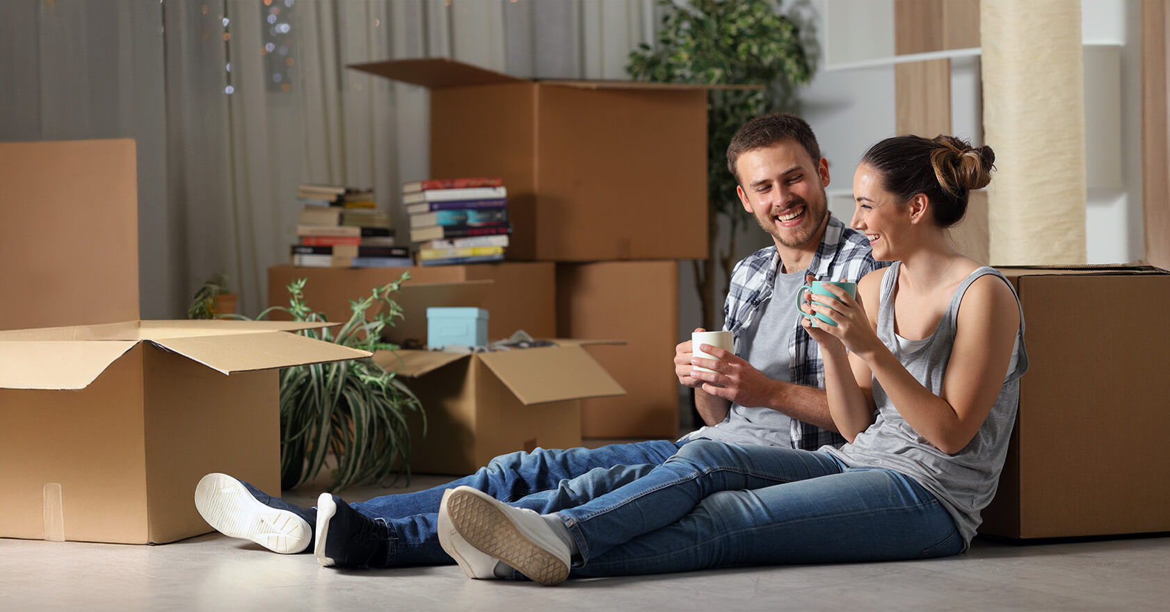 Two adults enjoying coffee together in their new home, surrounded by unpacked moving boxes.