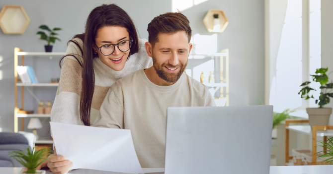 A woman and man, reviewing their a piece of paper and their laptop together.